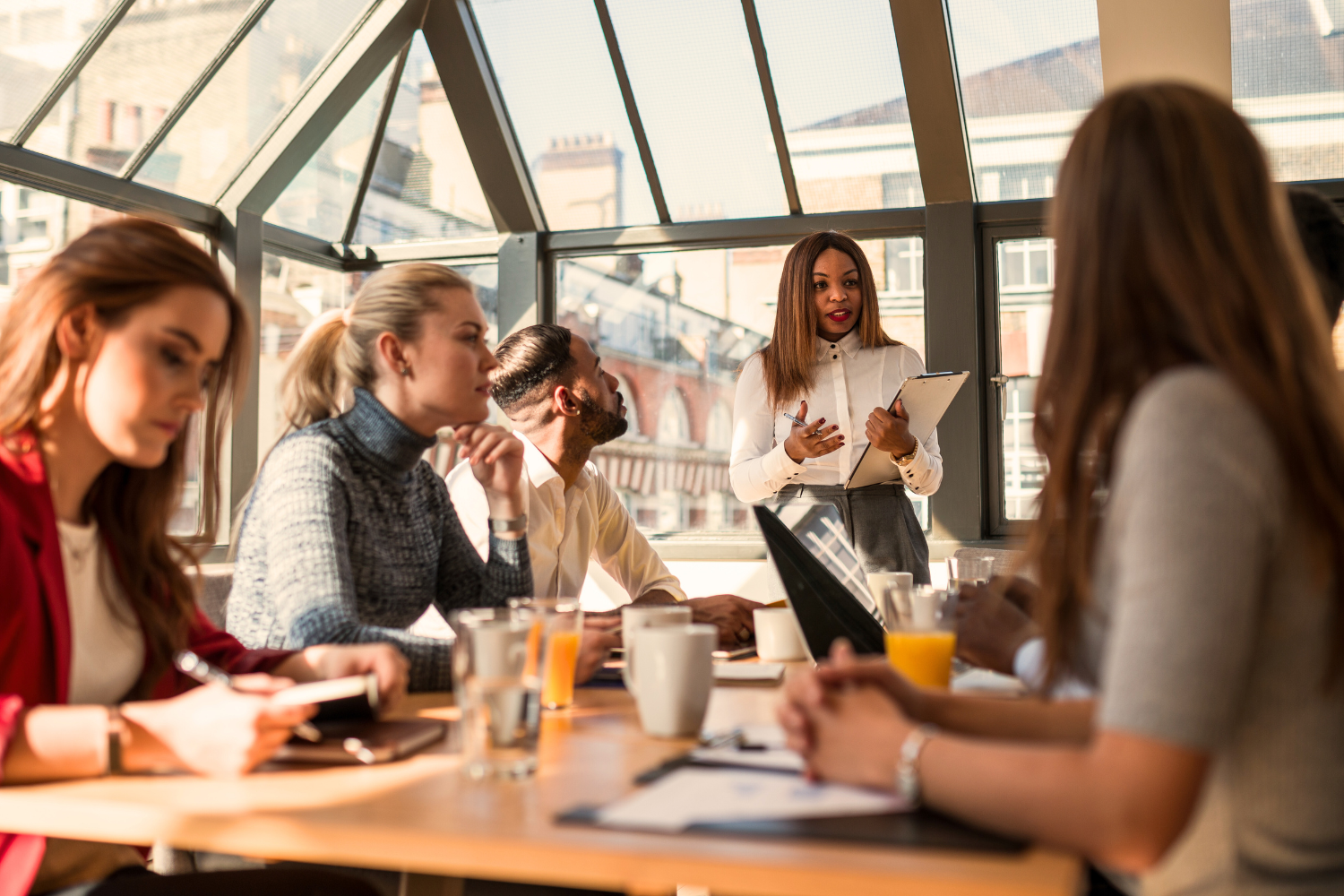 A workshop session at Clarity Holistic Therapy featuring a diverse group of individuals seated around a table, attentively listening to a woman leading the session in a bright, modern setting.